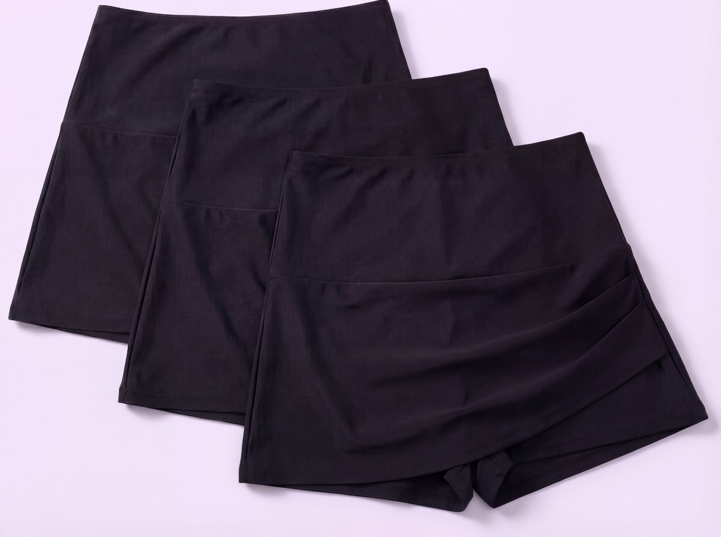 Three pairs of black shorts stacked on a white background